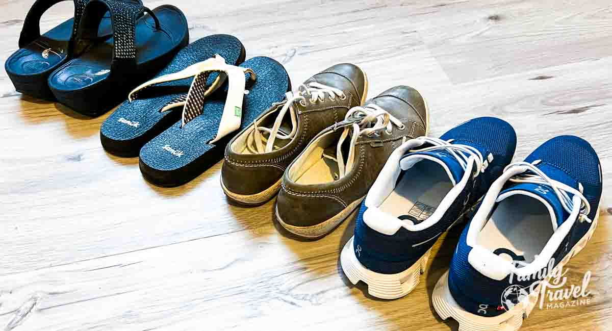Four pairs of shoes in a row - two sandals, one leather sneakers, one traditional sneakers. 