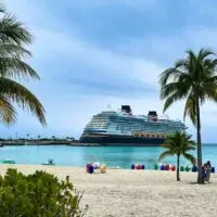 The Disney Wish docked at Castaway Cay with palm trees and water trikes in the foreground.