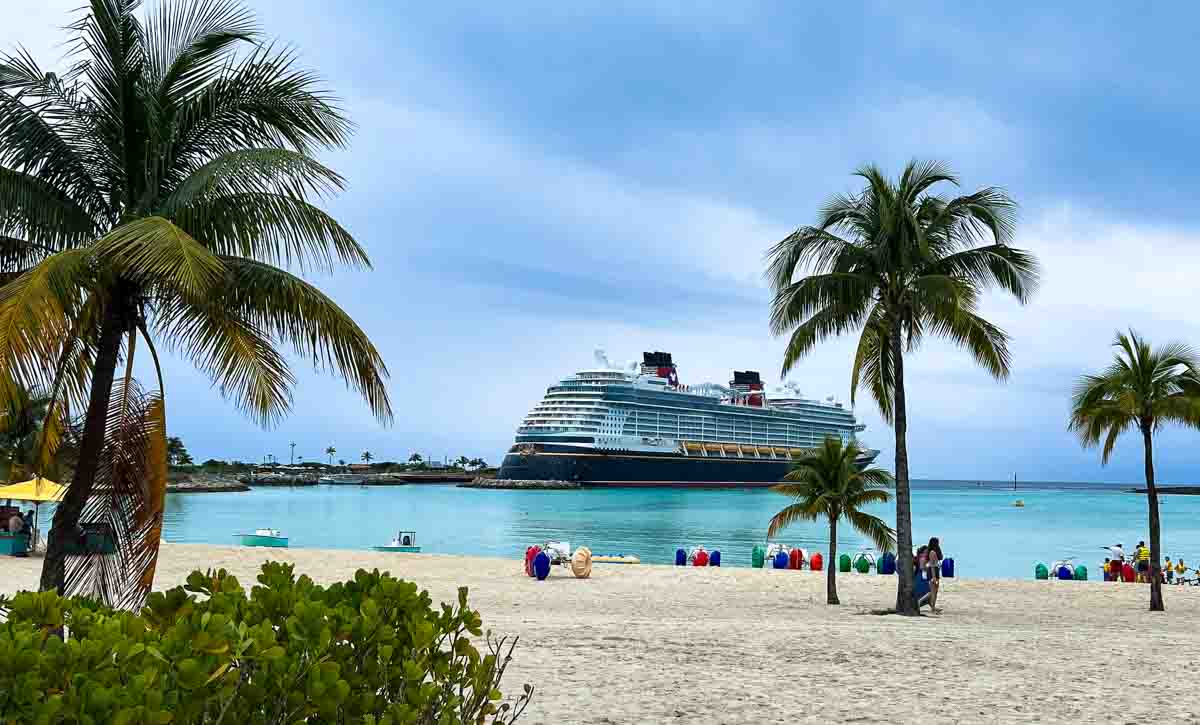 The Disney Wish docked at Castaway Cay with palm trees and water trikes in the foreground. 