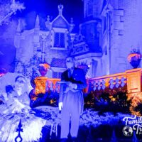 Spooky blue light at Haunted Mansion with butler and woman in dress with umbrella in the front.