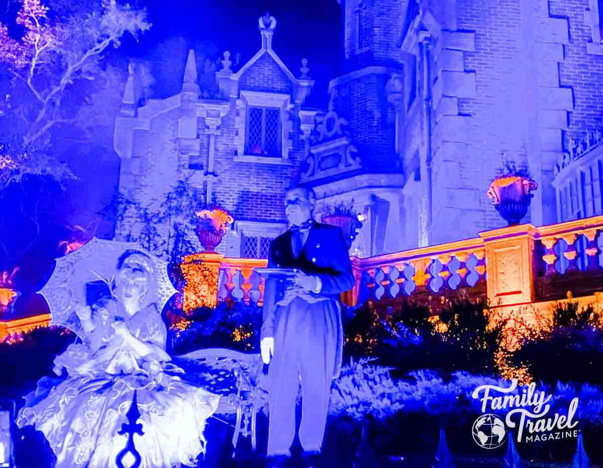 Spooky blue light at Haunted Mansion with butler and woman in dress with umbrella in the front. 