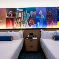 Two queen beds in a hotel with a Pixar themed mural above.