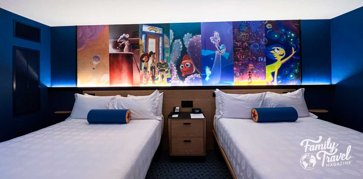 Two queen beds in a hotel with a Pixar themed mural above. 