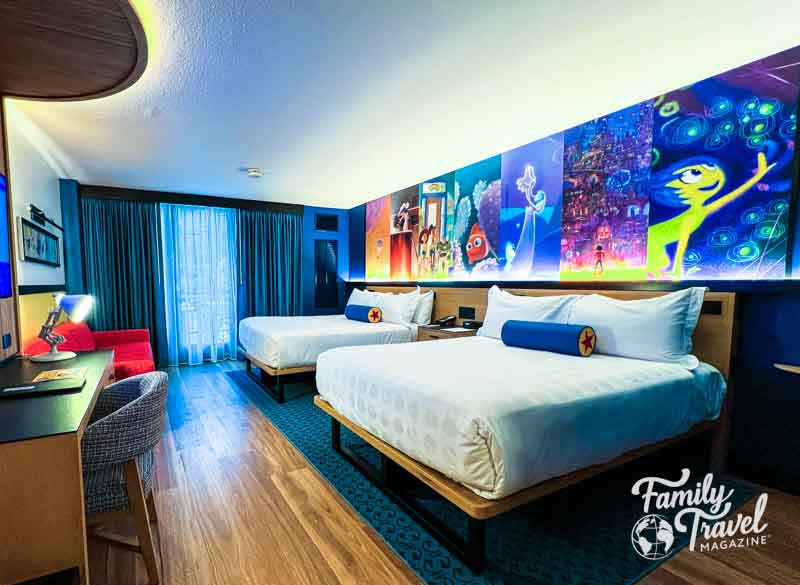 Room at Pixar Place Hotel with two queen beds, a couch, a desk, and a Pixar themed mural