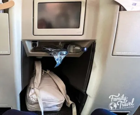 Beige backpack under seat in front in business class on airplane. 