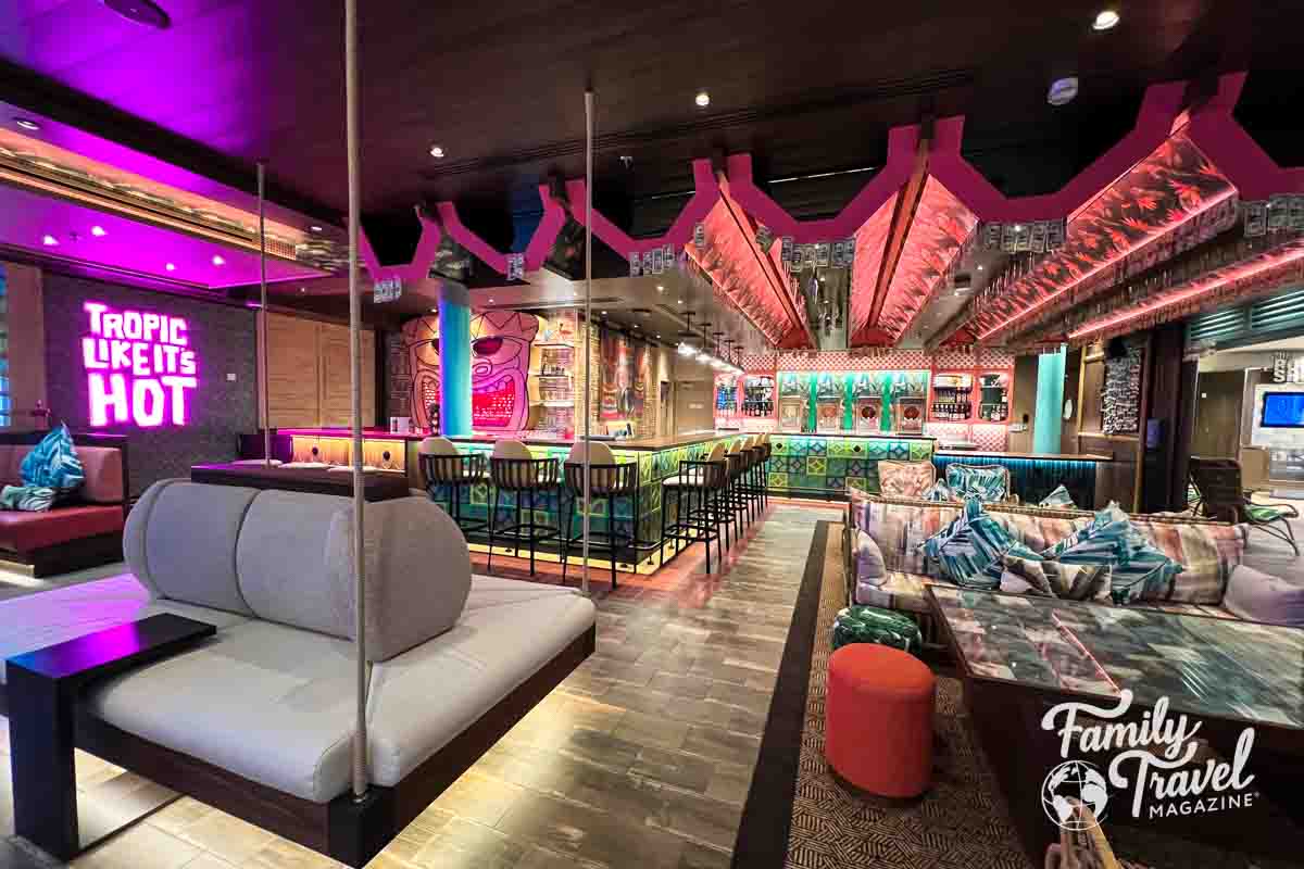 View of the Pesky Parrot tiki bar with colorful decor, hanging couches and other seating, and Tropic Like It's Hot sign.