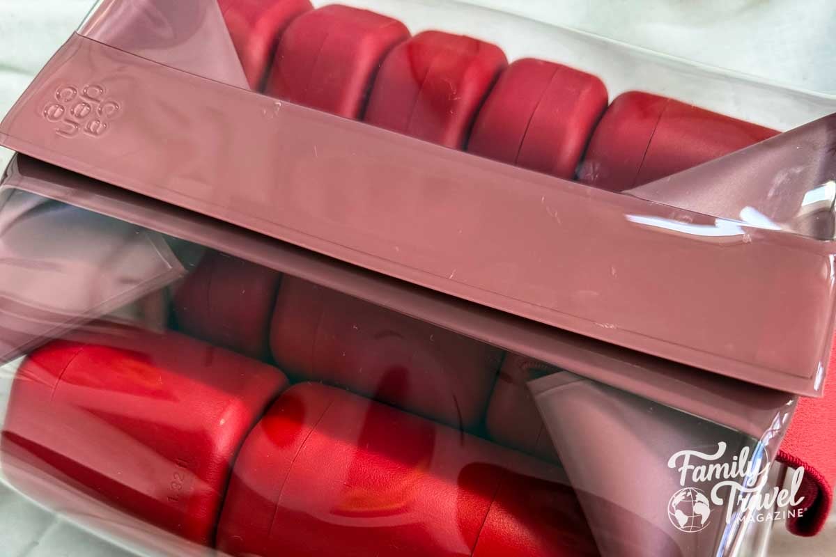 Red toiletry capsules in a clear and red bag. 