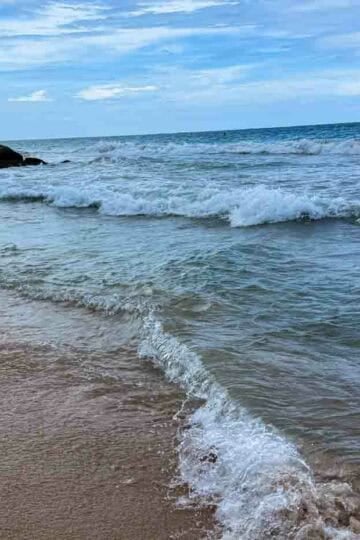 Waves gently rolling onto a sandy beach under a cloudy sky.