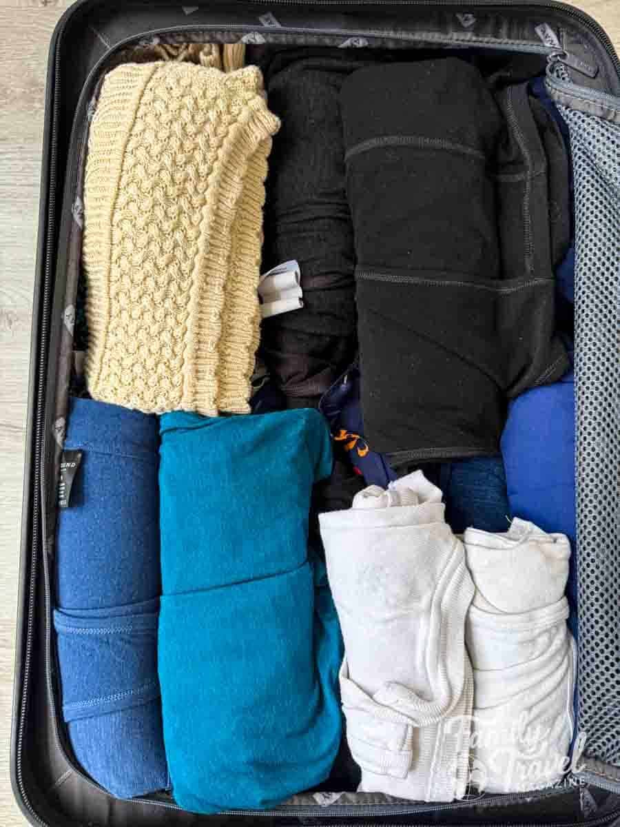 A black suitcase is efficiently packed with neatly folded and rolled clothes in various colors.