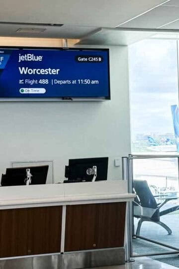 JetBlue departure gate at Orlando International Airport (MCO) for Flight 488 to Worcester, Massachusetts. Digital gate sign displays flight details and weather, with JetBlue aircraft visible through the terminal window. Family Travel Magazine watermark in corner.
