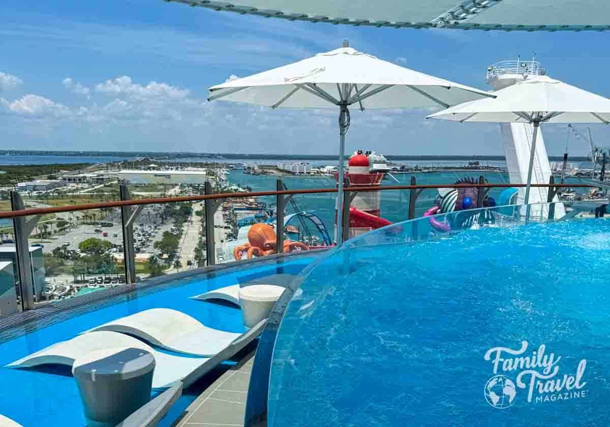 Infinity-edge pool and shaded lounge chairs on the suite sun deck aboard a Royal Caribbean cruise ship, with ocean views and waterslides in the background at Port Canaveral.