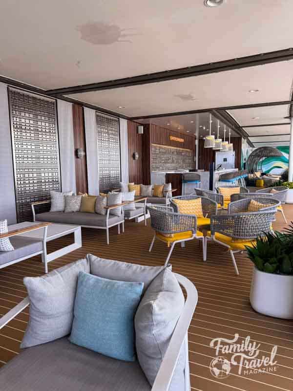 Stylish outdoor lounge area on the Royal Caribbean suite sun deck, featuring cushioned chairs, modern decor, and a bar with ocean-inspired accents.