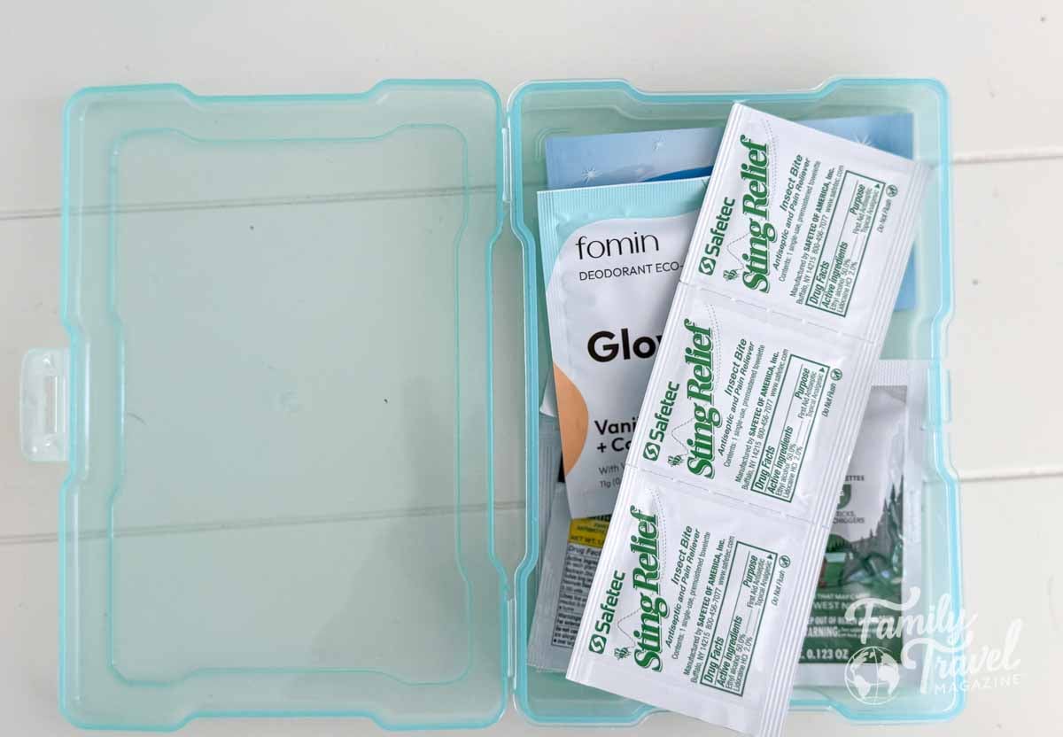 Travel essentials kit in a translucent blue case, containing insect bite sting relief wipes, deodorant wipes, and other personal care items—ideal for family vacations and packing convenience.
