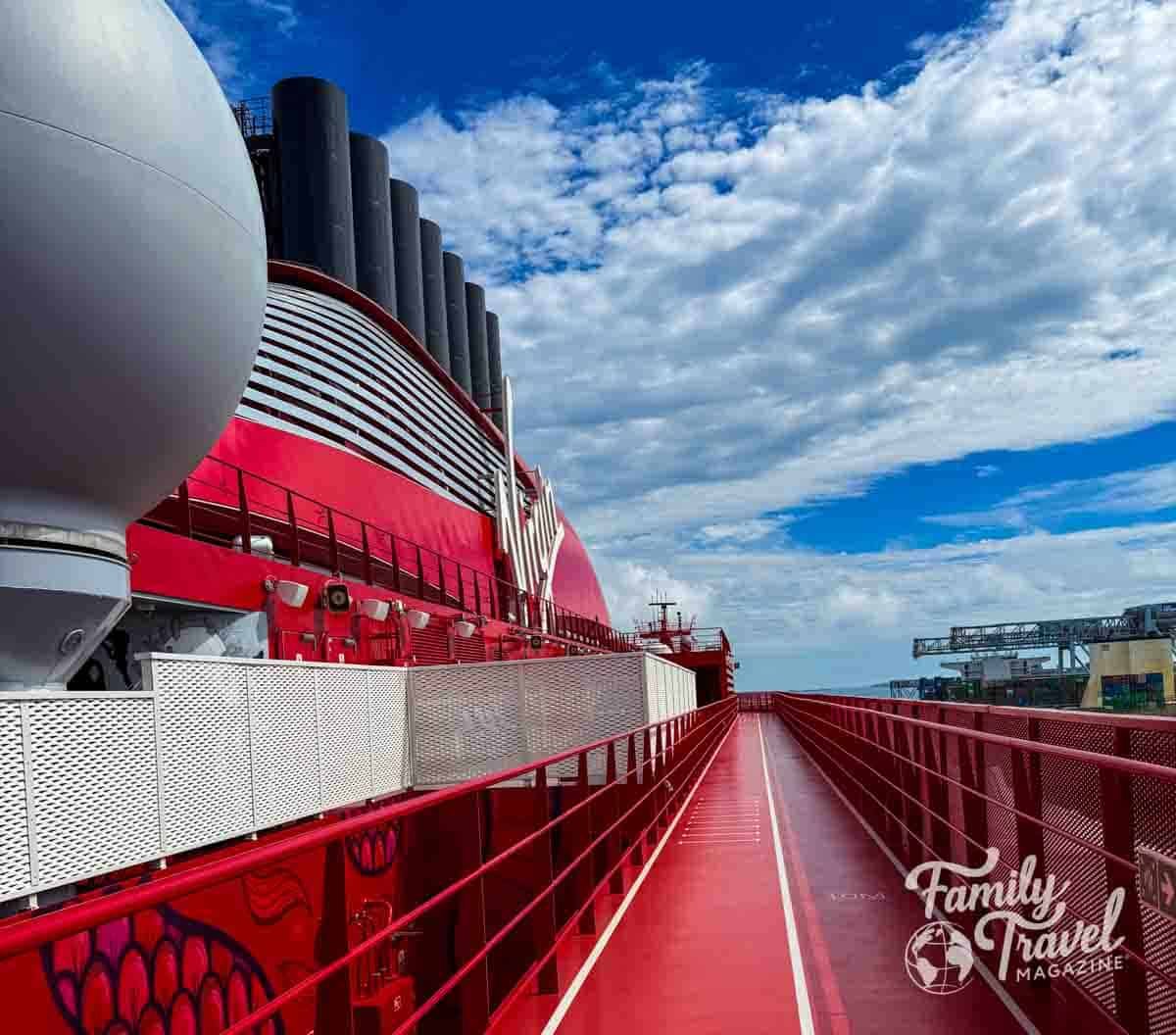 Running track on Virgin Voyages’ Brilliant Lady cruise ship with red deck, modern design, and ocean views under a bright blue sky.