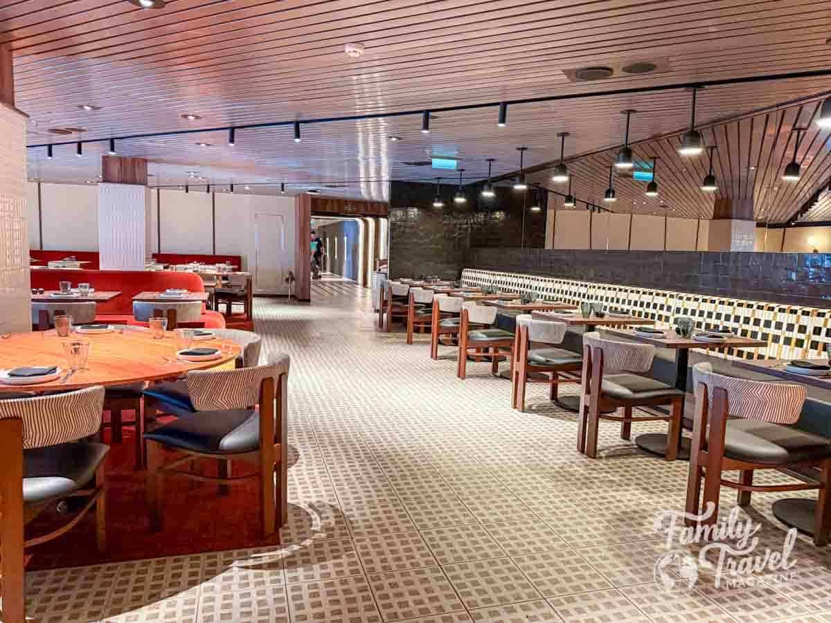Rojo by Razzle Dazzle restaurant on Virgin Voyages’ Brilliant Lady cruise ship with modern wood ceilings, red booths, and stylish dining tables.