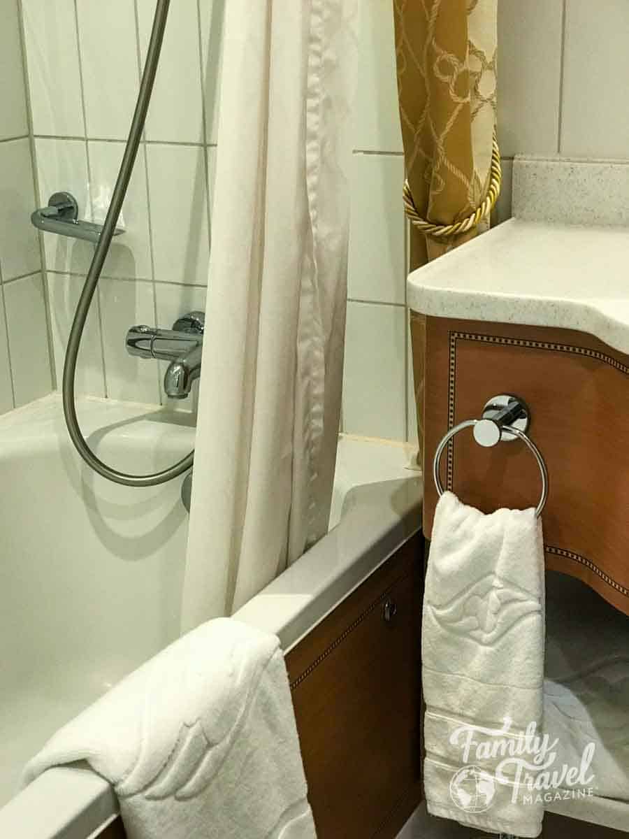 Disney Cruise Line stateroom bathroom with tub, shower, and nautical-style towels