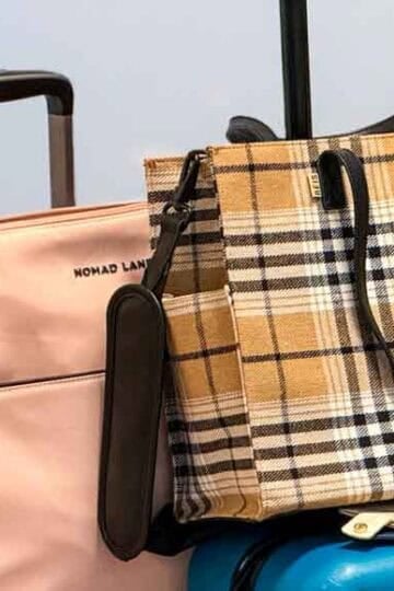Two stylish travel totes, a blush pink Nomad Lane bag and a tan plaid Beis tote, rest on top of a teal suitcase, perfect for organized carry-on travel.