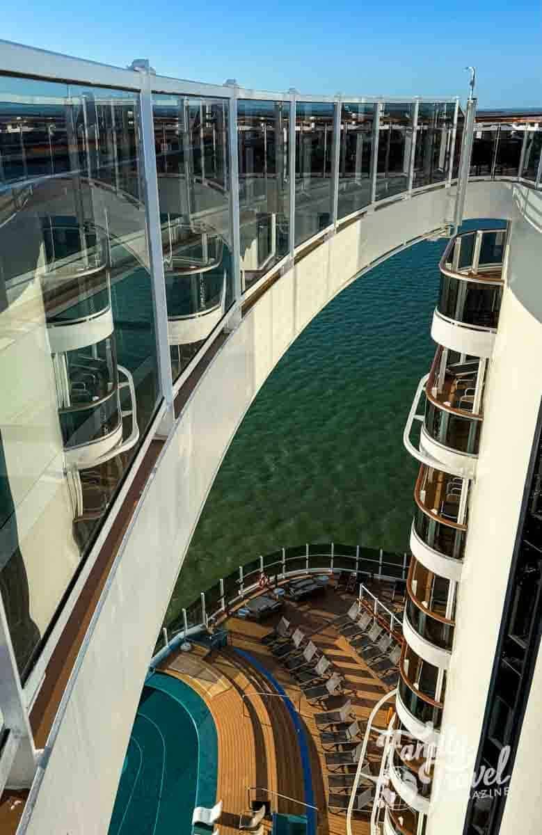 Cruise ship deck with lounge chairs and glass walkway over water.