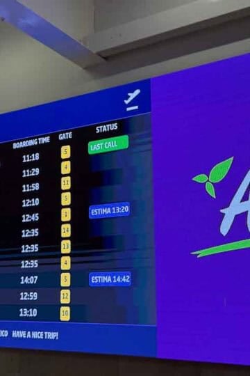 Airport departures board in Puerto Vallarta showing flight times and gates beside an AeroMexico ad.
