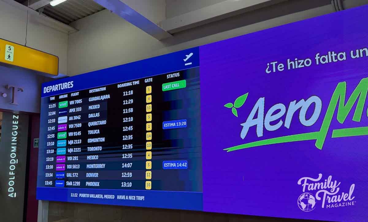 Airport departures board in Puerto Vallarta showing flight times and gates beside an AeroMexico ad.