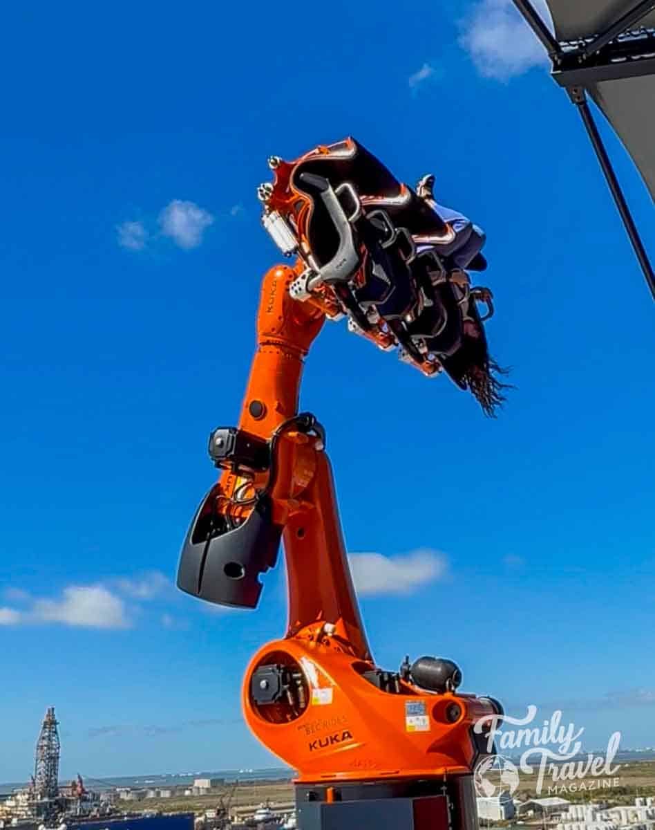 Orange robotic arm holding riders against a blue sky.