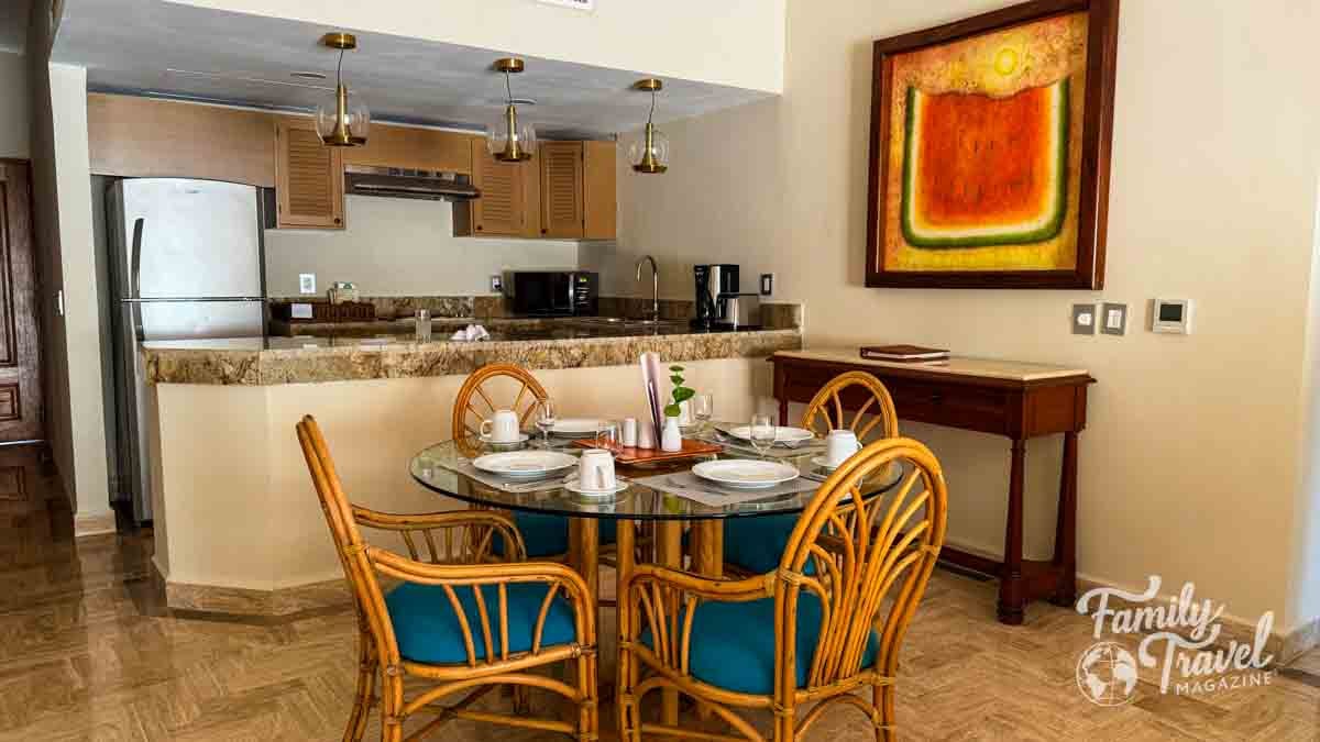 Suite dining area and kitchen at Velas Vallarta with rattan chairs, granite countertops, and warm decor.
