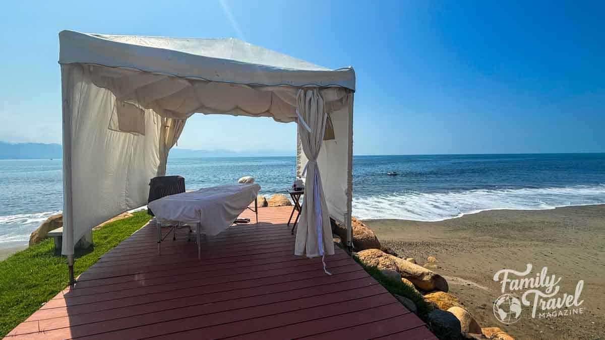 White tented massage cabana on a wooden deck by the ocean at Velas Vallarta, offering a tranquil seaside spa experience.