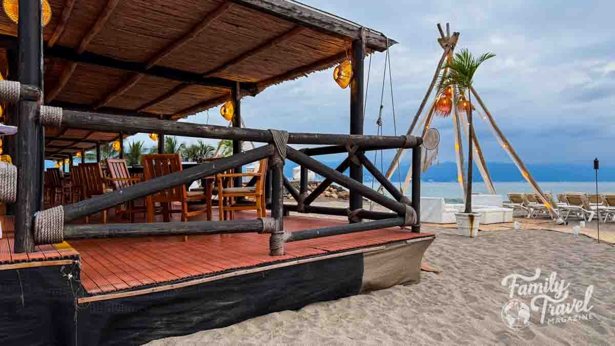 Beachfront wooden restaurant deck with lantern lighting at Velas Vallarta in Puerto Vallarta, overlooking the ocean with lounge chairs on the sand.