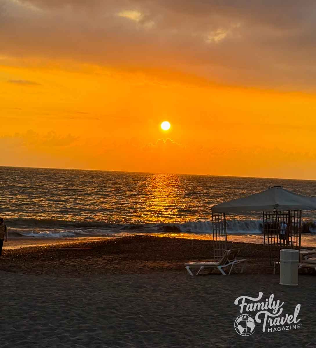 Golden sunset over the ocean at Velas Vallarta beach with lounge chairs and a canopy on the sand.