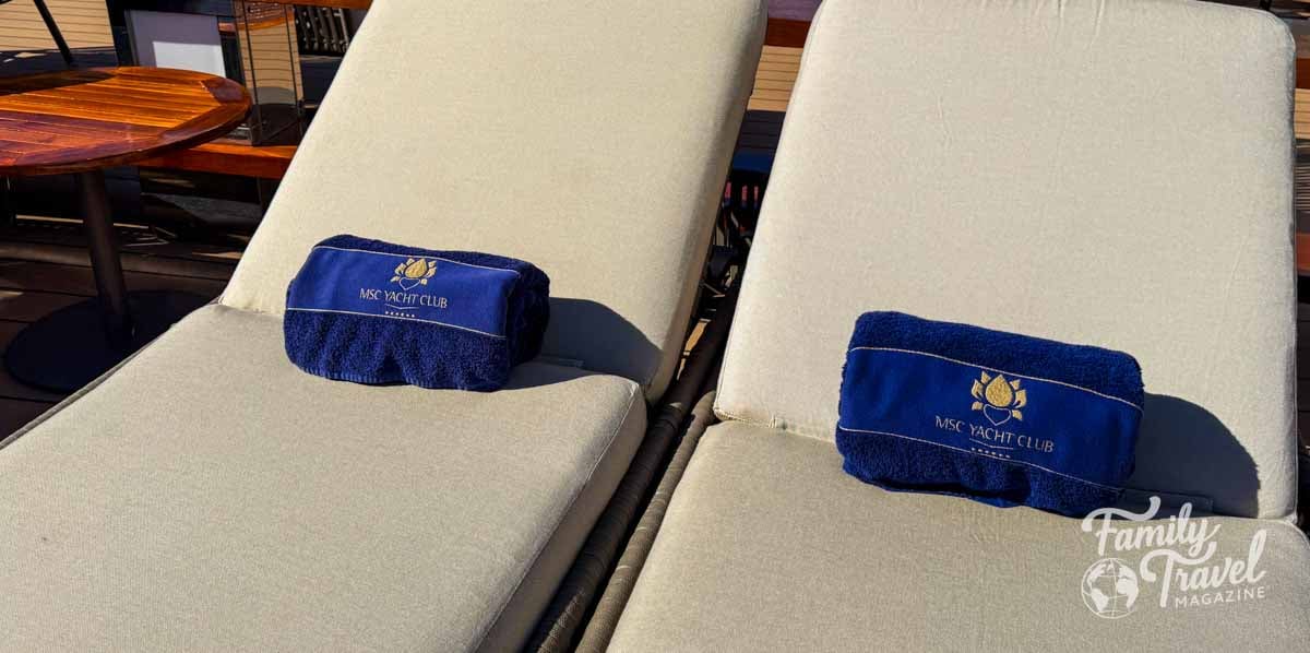 Two lounge chairs with blue MSC Yacht Club towels sit side by side.