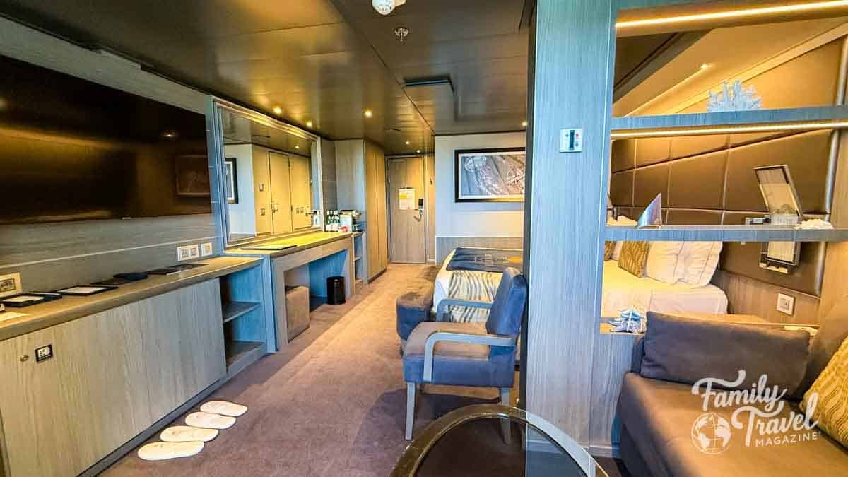 Cruise ship cabin interior with bed, seating, and vanity area.