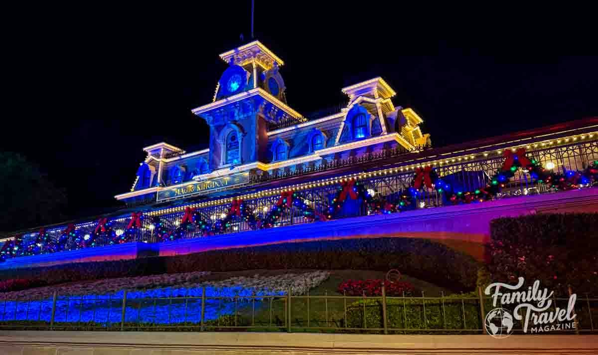 Magic Kingdom train station illuminated with holiday decorations at night.