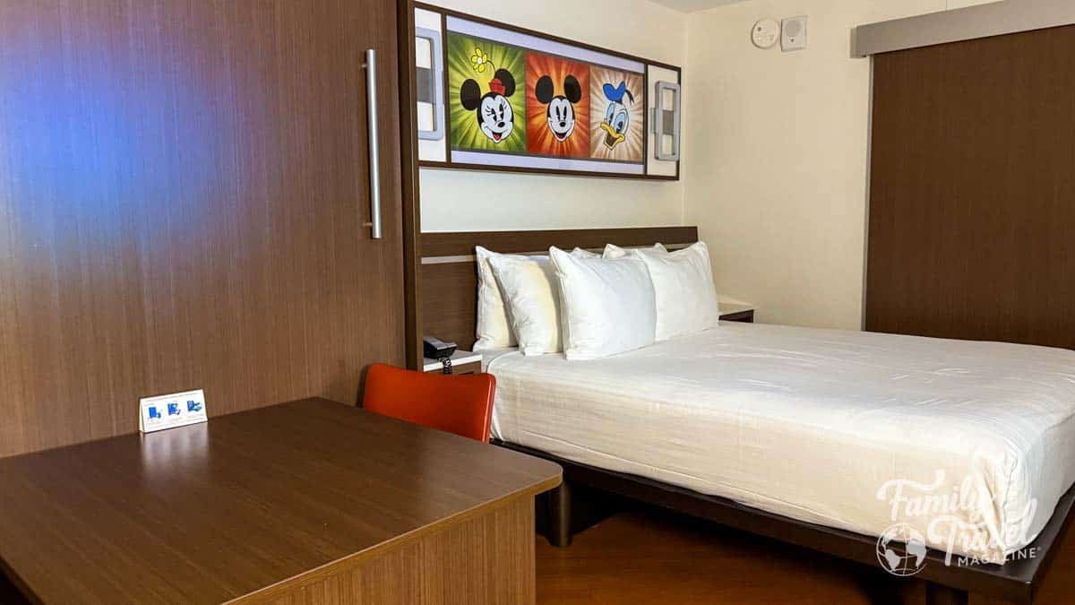 Hotel room featuring a bed with white linens and a table/murphy bed with Disney character art.