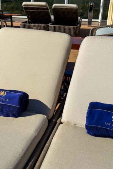 Two lounge chairs with blue towels sit on a wooden deck.