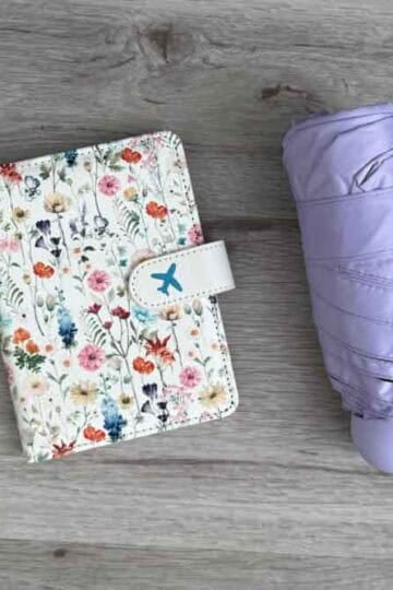 A flat lay of a succulent, floral passport holder, purple umbrella, and bear-shaped portable fan.