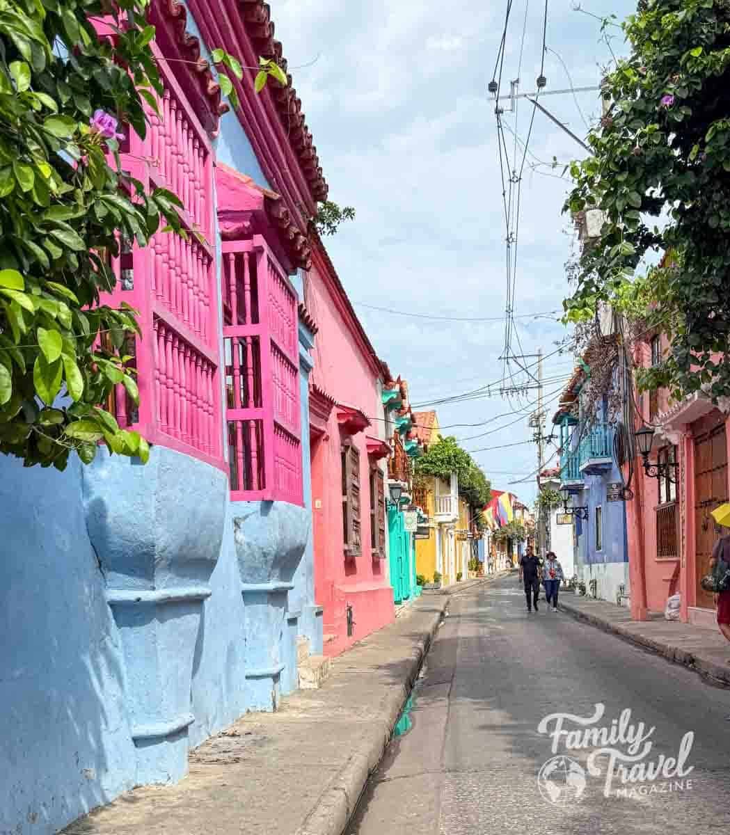 A vibrant street in Cartagena, Colombia, lined with colorful colonial buildings and balconies under a bright sky.