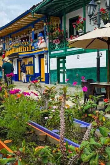 Lively street scene in Salento, Colombia, featuring colorful buildings, outdoor cafes, and vibrant flower planters.