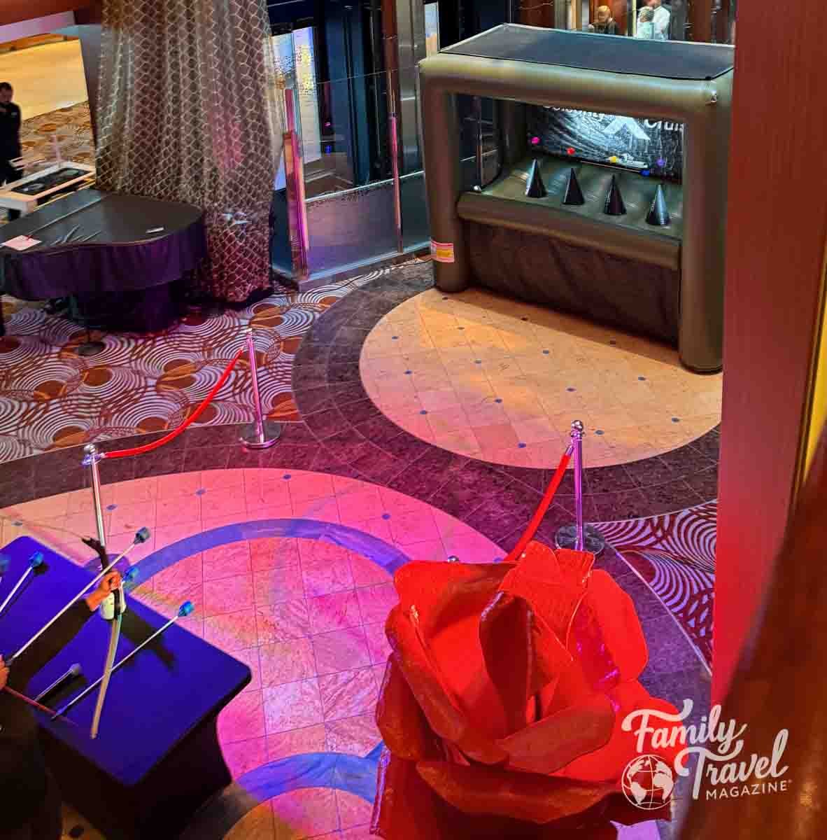 A cruise ship atrium with an archery game, arrows on a table, and a large red rose decoration.