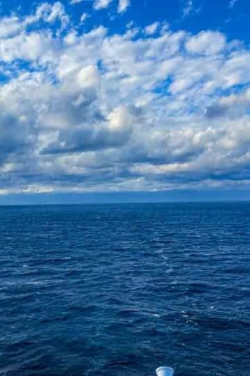 Expansive deep blue ocean under a dramatic sky with white and grey clouds.