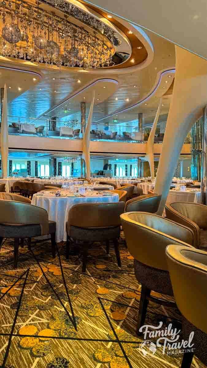 Multi-level main dining room with ornate chandeliers and set tables on a Celebrity cruise ship