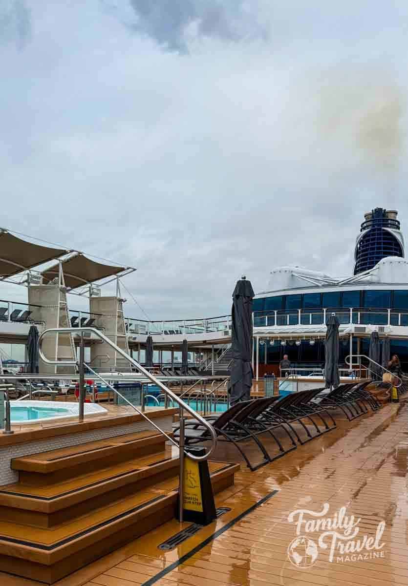 Rainy pool deck on a Celebrity Cruises ship with lounge chairs, a hot tub, and its distinctive blue funnel.