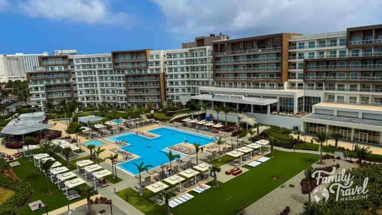 Aerial view of the Embassy Suites hotel in Aruba, featuring multiple pools, lounge chairs, and palm trees.