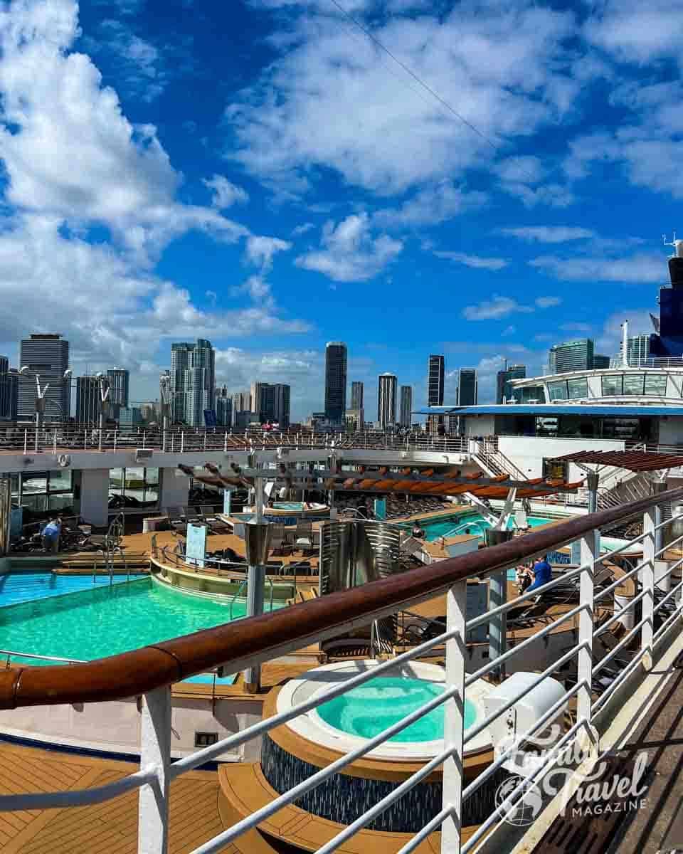 Cruise ship deck with turquoise pools and hot tubs overlooking the Miami, Florida skyline.