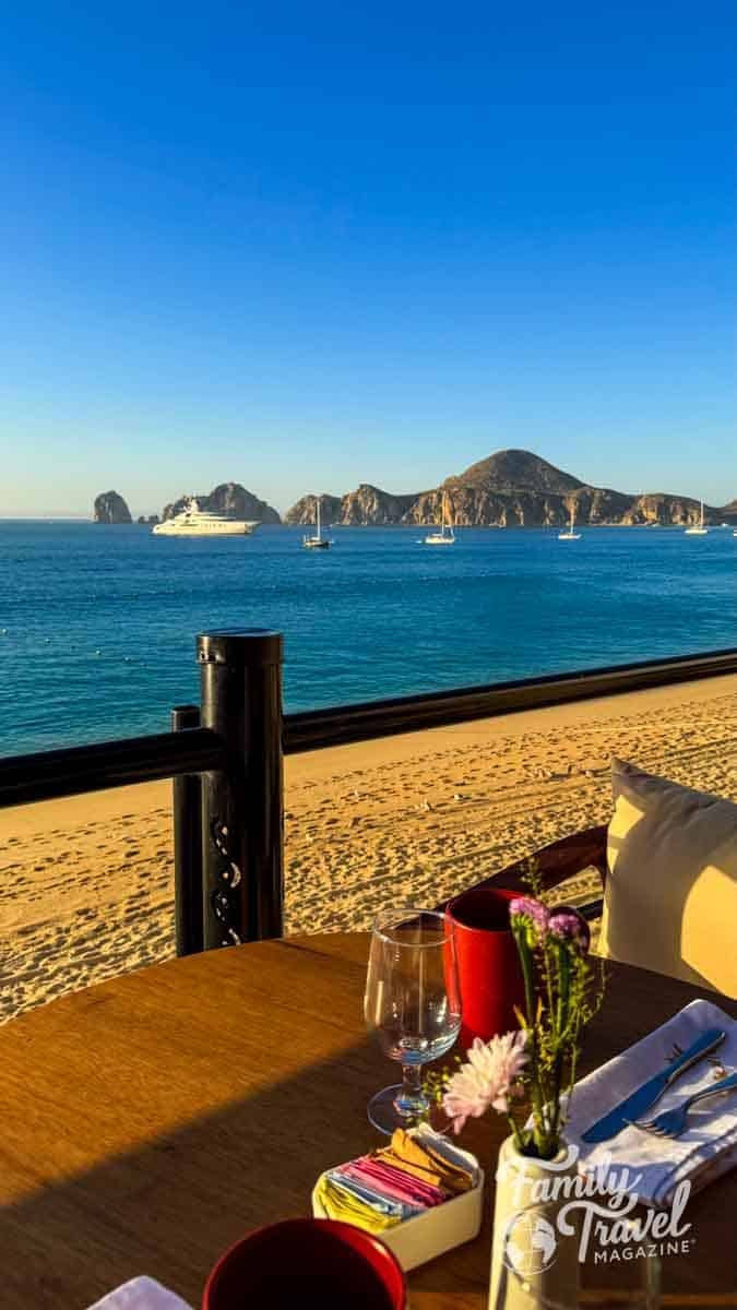 Dining table overlooking El Arco de Cabo San Lucas, boats on the blue ocean, and a sandy beach.