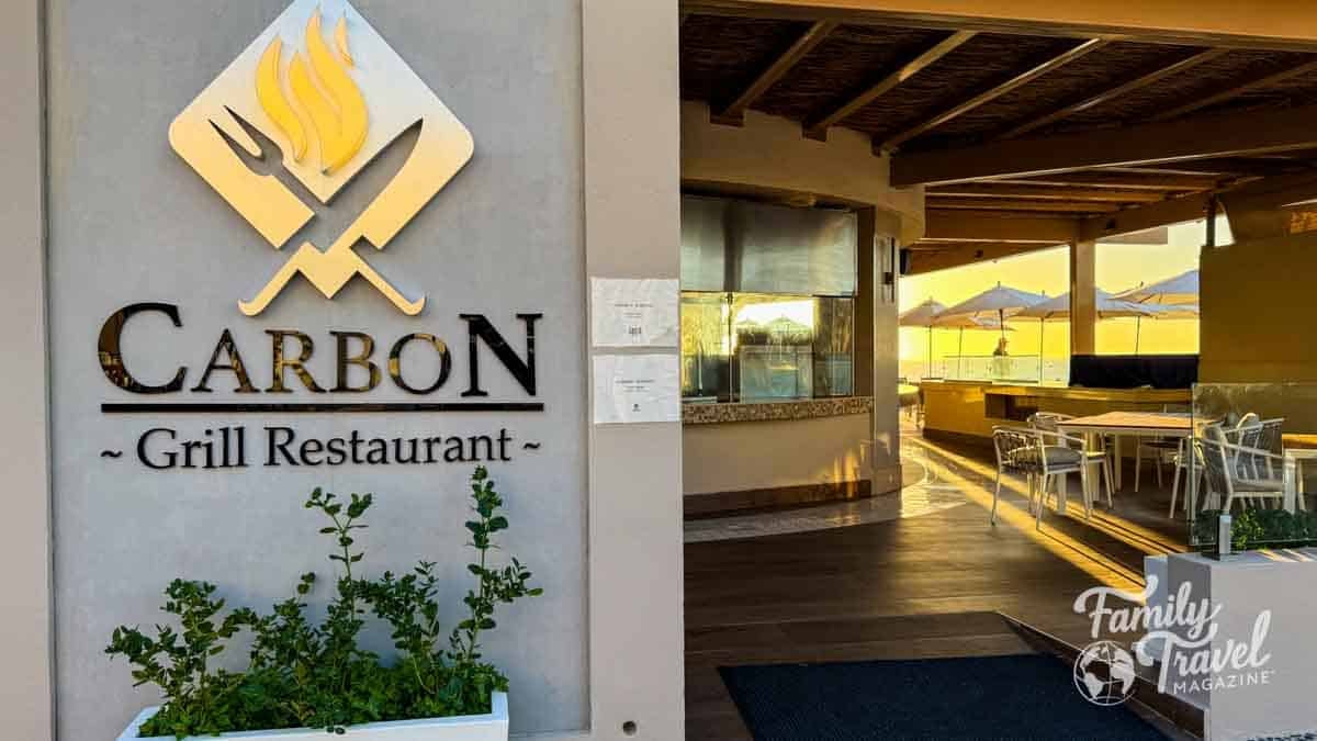 CARBON Grill Restaurant sign next to an inviting outdoor dining area with umbrellas at sunset.