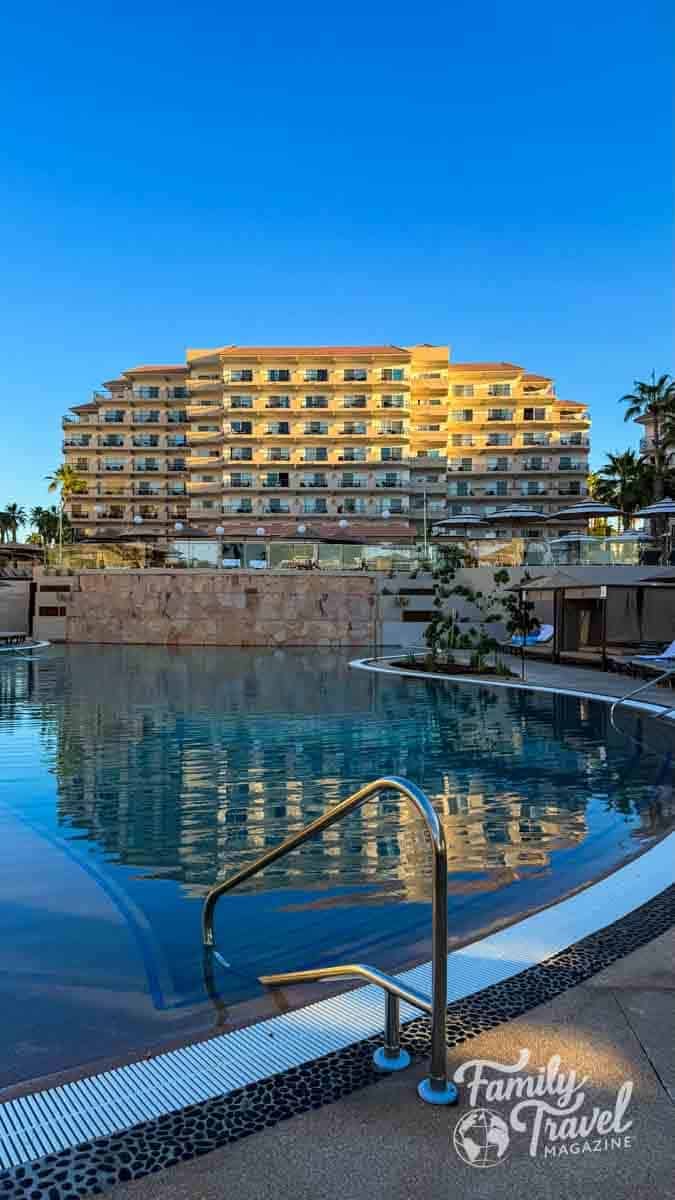 The terraced Villa del Palmar Los Cabos resort building overlooks a sparkling blue swimming pool on a sunny day.