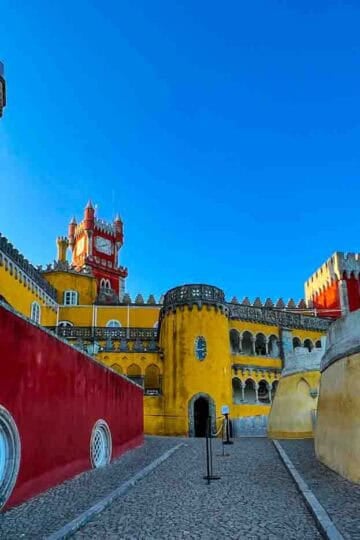 The colorful Pena Palace in Sintra, Portugal, with its iconic clock tower and battlements under a clear blue sky.