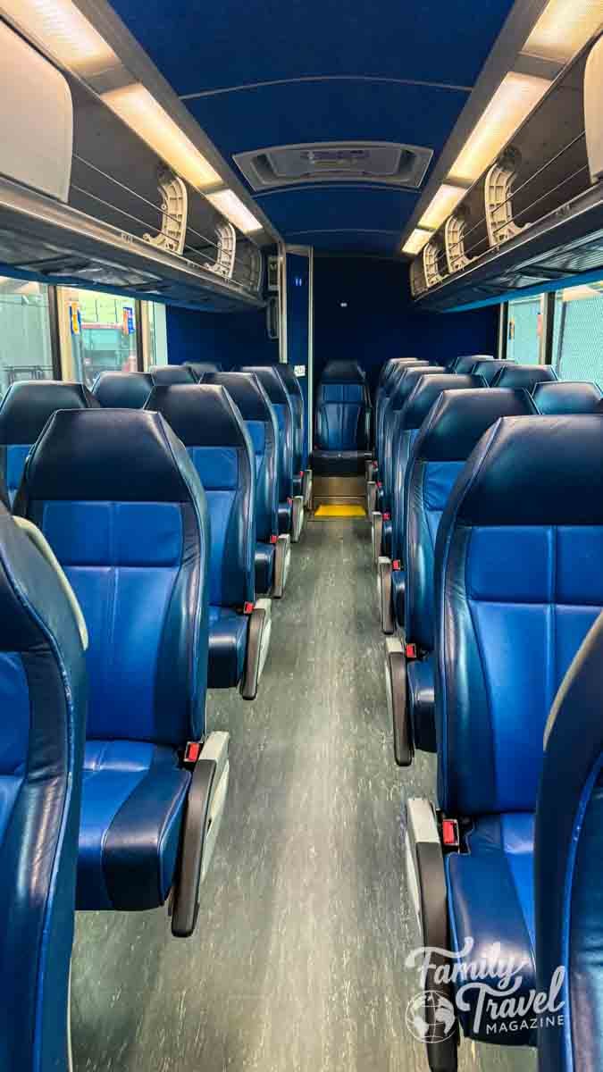 Clean, empty coach bus interior with rows of blue seats and overhead storage.
