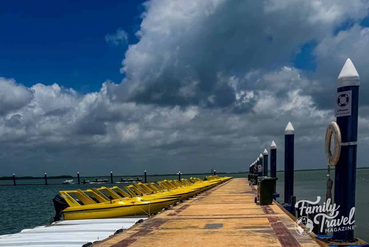 Yellow speedboats line a pier in Cancun, Mexico, under a cloudy sky, ready for family travel adventures.