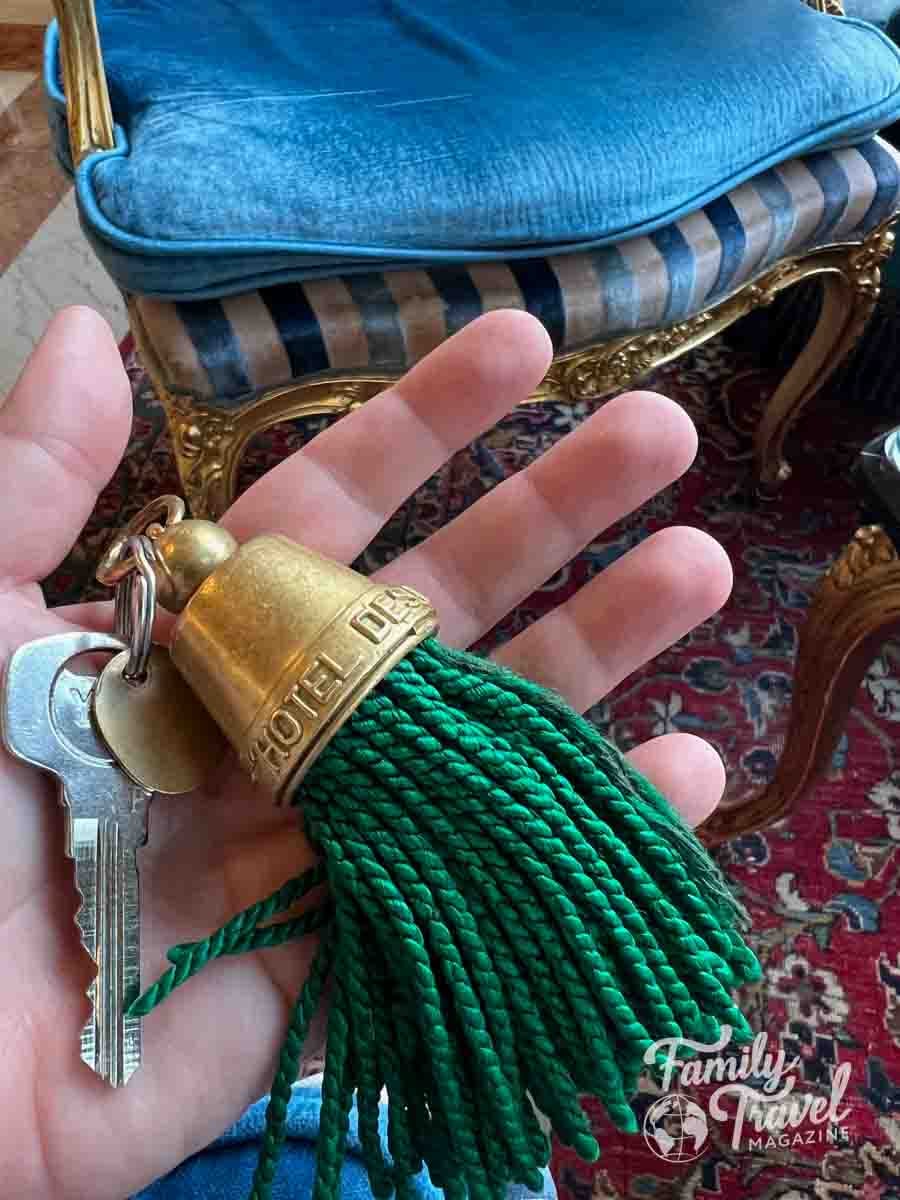 Hand holding a large key from a hotel, featuring a green tassel.